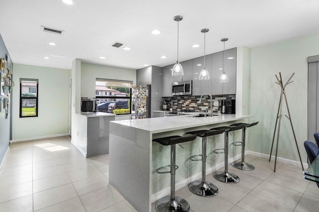 kitchen featuring kitchen peninsula, pendant lighting, appliances with stainless steel finishes, sink, and gray cabinetry