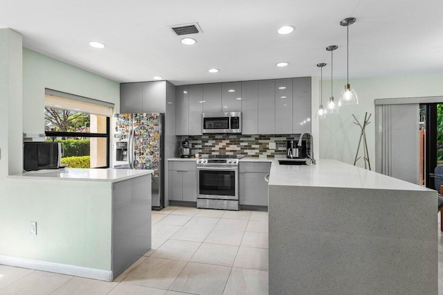 kitchen featuring kitchen peninsula, pendant lighting, sink, gray cabinets, and stainless steel appliances