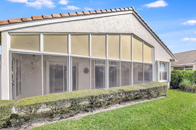 rear view of house featuring a tiled roof, stucco siding, a lawn, and a sunroom