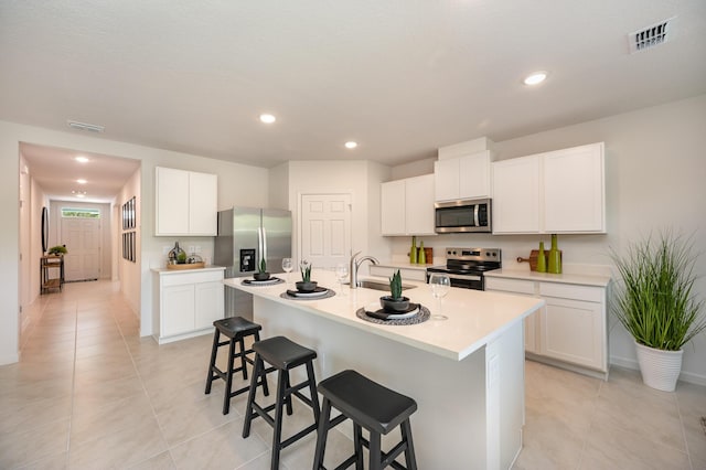 kitchen with visible vents, appliances with stainless steel finishes, a kitchen island with sink, light countertops, and a breakfast bar area