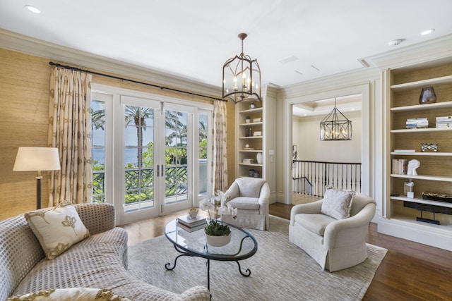 living room with built in shelves, hardwood / wood-style floors, a water view, and a notable chandelier