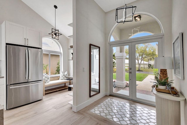 foyer with high vaulted ceiling, a wealth of natural light, an inviting chandelier, and light hardwood / wood-style floors