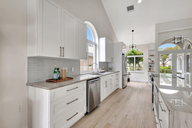 kitchen featuring pendant lighting, white cabinetry, sink, light stone counters, and stainless steel appliances