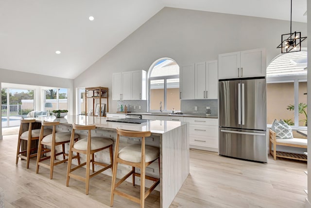 kitchen featuring stainless steel fridge, a breakfast bar, backsplash, high vaulted ceiling, and a center island