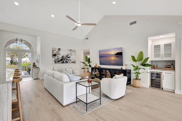 living room with bar area, high vaulted ceiling, light hardwood / wood-style flooring, ceiling fan, and beverage cooler