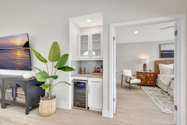 bar with white cabinets, light hardwood / wood-style flooring, beverage cooler, and decorative backsplash