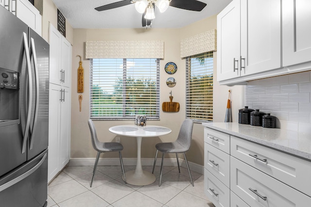 kitchen with white cabinetry, light tile patterned floors, stainless steel fridge, light stone countertops, and decorative backsplash