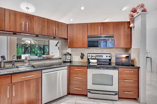 kitchen featuring appliances with stainless steel finishes, dark stone counters, tasteful backsplash, sink, and light tile patterned floors