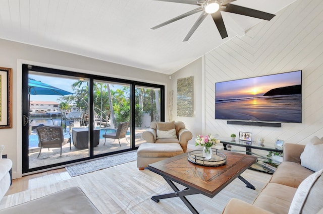 living room with ceiling fan, lofted ceiling, light wood-type flooring, and wood walls