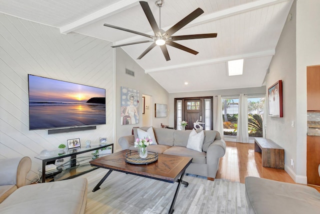 living room with ceiling fan, beam ceiling, high vaulted ceiling, light wood-type flooring, and wood walls