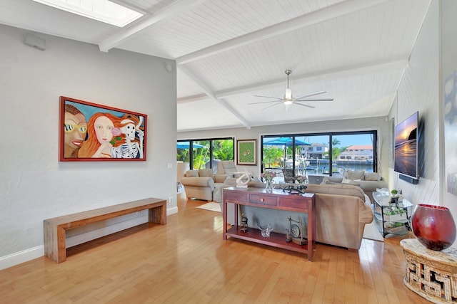 living room featuring ceiling fan, vaulted ceiling with skylight, and light wood-type flooring