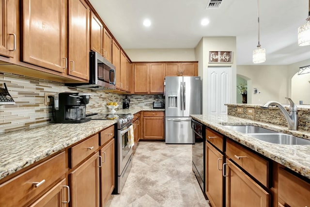 kitchen featuring pendant lighting, appliances with stainless steel finishes, sink, backsplash, and light stone counters