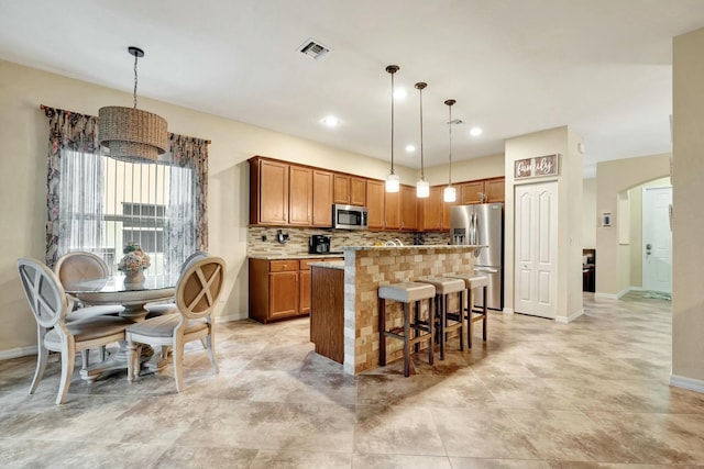 kitchen with appliances with stainless steel finishes, tasteful backsplash, hanging light fixtures, a kitchen island, and a breakfast bar