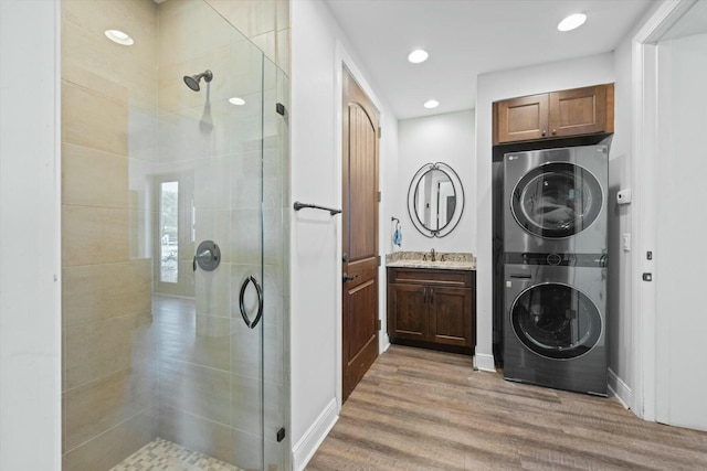 bathroom with vanity, stacked washing maching and dryer, a shower with door, and hardwood / wood-style floors