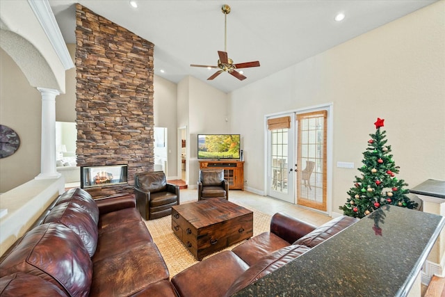 living room featuring ornate columns, a stone fireplace, a towering ceiling, ceiling fan, and french doors