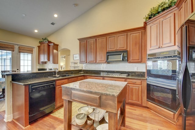 kitchen with sink, a center island, dark stone countertops, light hardwood / wood-style floors, and black appliances