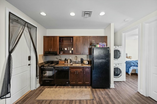 kitchen with stacked washer and clothes dryer, sink, dark hardwood / wood-style floors, stone counters, and black appliances