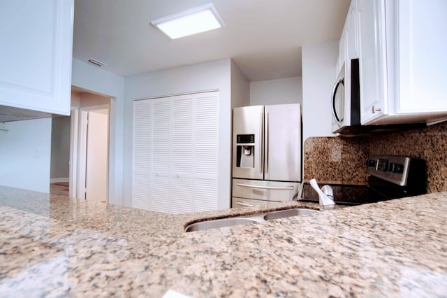 kitchen with light stone countertops, white cabinetry, appliances with stainless steel finishes, and tasteful backsplash