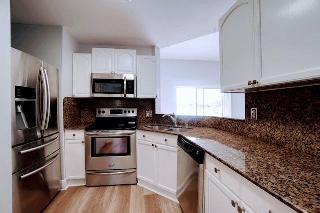 kitchen featuring light hardwood / wood-style flooring, appliances with stainless steel finishes, sink, white cabinetry, and dark stone counters