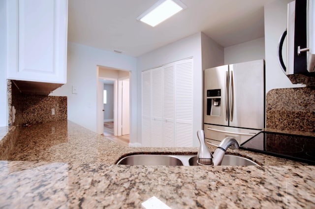 kitchen featuring stainless steel refrigerator with ice dispenser, sink, white cabinetry, and light stone counters