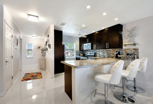 kitchen featuring a breakfast bar area, tasteful backsplash, light stone counters, appliances with stainless steel finishes, and kitchen peninsula