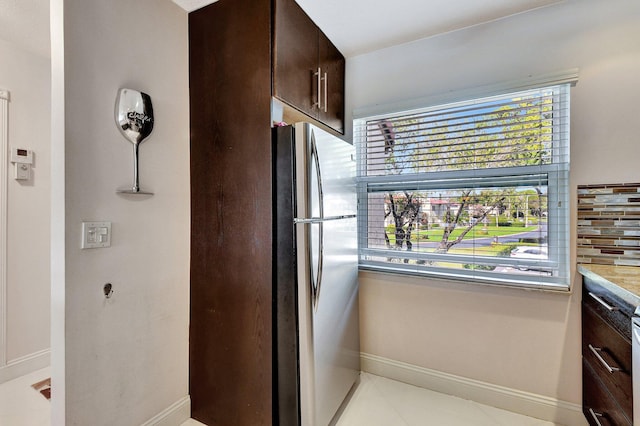 kitchen with stainless steel refrigerator, light tile patterned flooring, dark brown cabinets, and backsplash