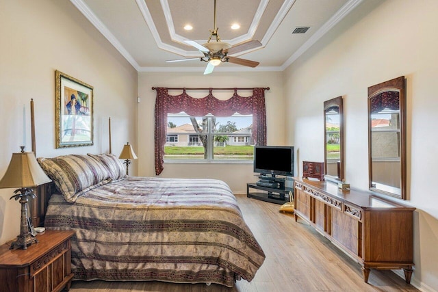 bedroom with ceiling fan, a tray ceiling, crown molding, and light wood-type flooring