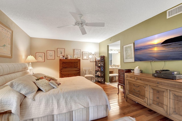 bedroom featuring connected bathroom, a textured ceiling, light hardwood / wood-style flooring, and ceiling fan