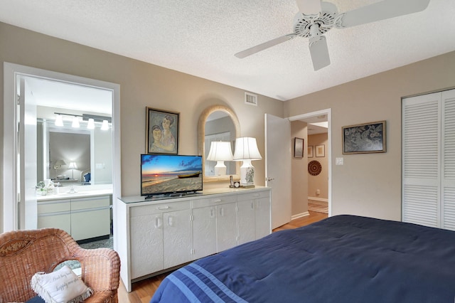 bedroom with light hardwood / wood-style flooring, ceiling fan, connected bathroom, a textured ceiling, and a closet