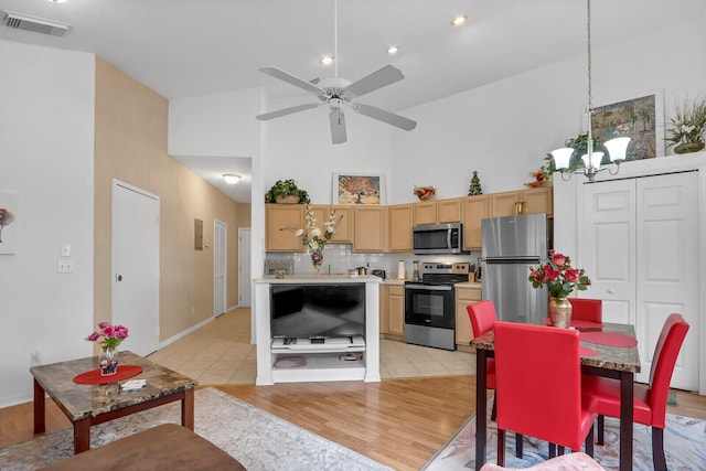 kitchen with a high ceiling, appliances with stainless steel finishes, light brown cabinetry, backsplash, and light wood-type flooring