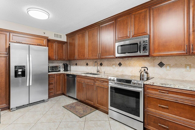 kitchen with light tile patterned floors, light stone countertops, sink, and appliances with stainless steel finishes