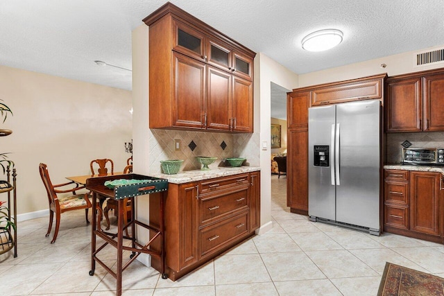 kitchen with stainless steel refrigerator with ice dispenser, light tile patterned floors, light stone counters, and decorative backsplash