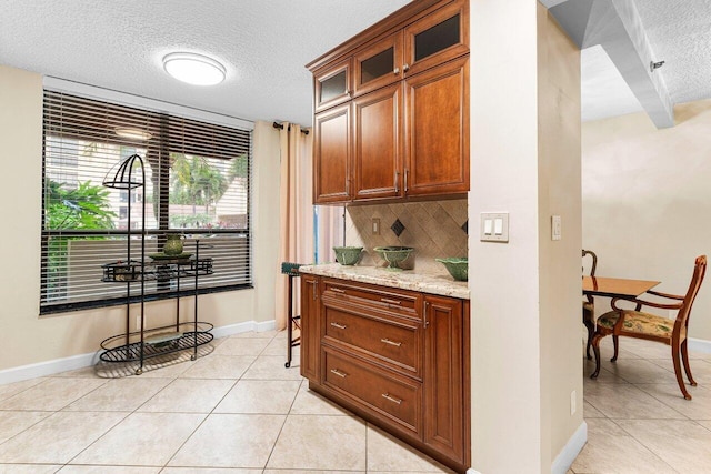 kitchen featuring glass insert cabinets, a textured ceiling, baseboards, backsplash, and light tile patterned flooring