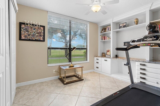 exercise area with light tile patterned floors, baseboards, ceiling fan, and a textured ceiling