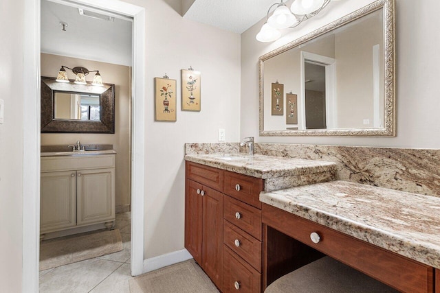 bathroom featuring baseboards, tile patterned flooring, two vanities, and a sink