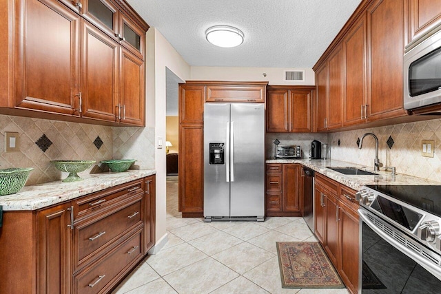 kitchen featuring appliances with stainless steel finishes, sink, backsplash, light tile patterned floors, and light stone countertops