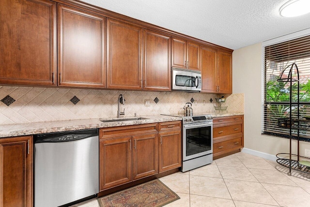 kitchen with appliances with stainless steel finishes, sink, backsplash, light tile patterned floors, and light stone counters