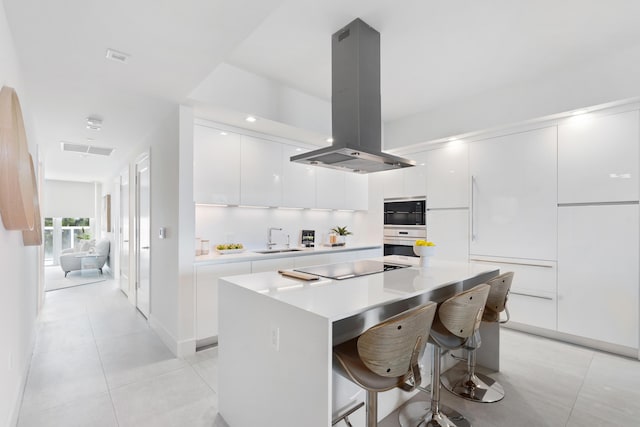 kitchen with visible vents, island range hood, modern cabinets, black electric stovetop, and a sink