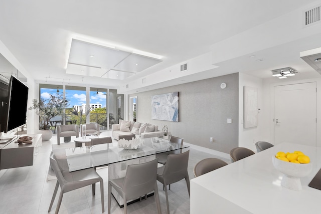 dining room featuring a tray ceiling, a wall of windows, visible vents, and baseboards