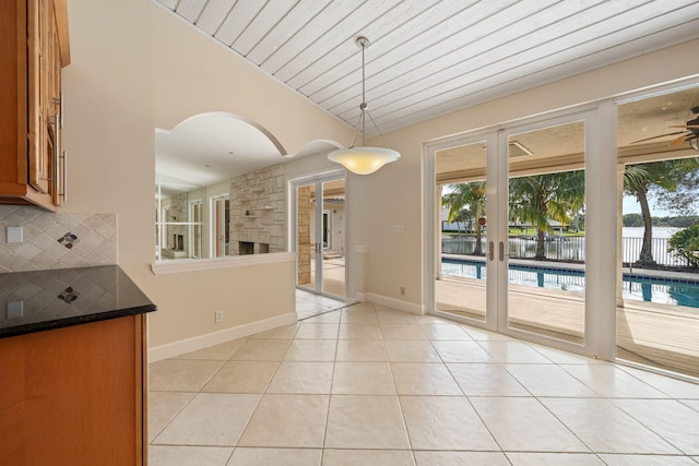 interior space with vaulted ceiling, decorative backsplash, hanging light fixtures, light tile patterned floors, and plenty of natural light