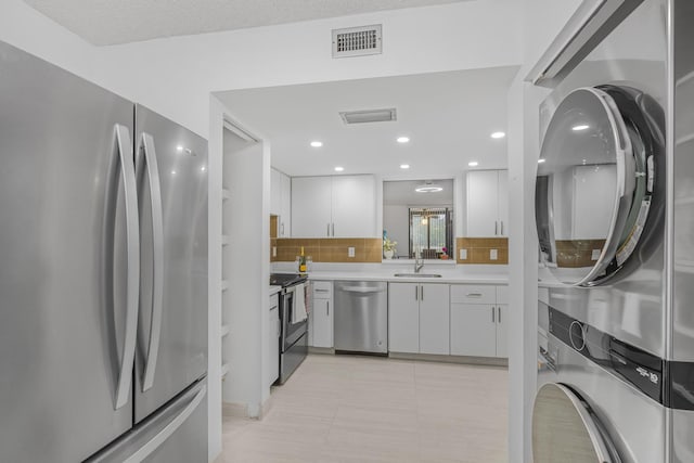 kitchen with sink, stacked washer / dryer, white cabinets, stainless steel appliances, and backsplash