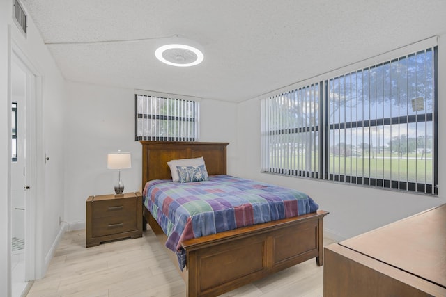 bedroom featuring multiple windows, a textured ceiling, and light wood-type flooring