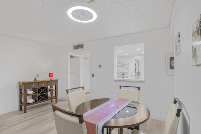 dining space with light wood-type flooring and a textured ceiling