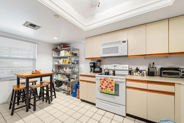 kitchen with cream cabinetry, white appliances, ornamental molding, and a tray ceiling