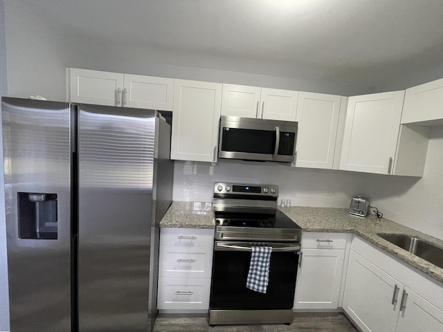 kitchen with appliances with stainless steel finishes, white cabinetry, sink, dark wood-type flooring, and light stone counters