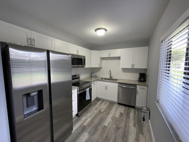 kitchen with light stone countertops, white cabinets, wood-type flooring, stainless steel appliances, and sink