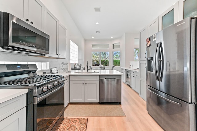 kitchen featuring wine cooler, sink, appliances with stainless steel finishes, kitchen peninsula, and light hardwood / wood-style floors