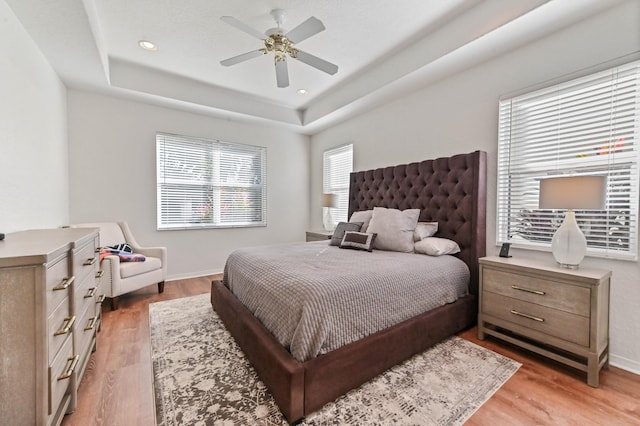 bedroom with light hardwood / wood-style flooring, ceiling fan, and a tray ceiling