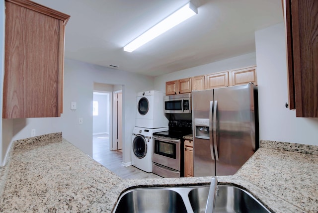 kitchen featuring sink, light stone countertops, stacked washer and dryer, light hardwood / wood-style floors, and stainless steel appliances