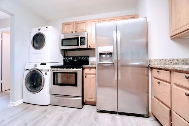 kitchen featuring light brown cabinetry, appliances with stainless steel finishes, light stone countertops, stacked washer / dryer, and light hardwood / wood-style floors